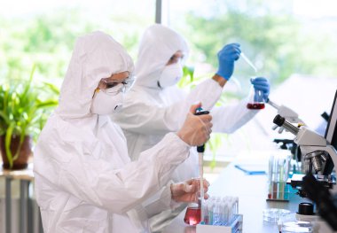 Laboratuvarda çalışan koruyucu giysi ve maskeli bilim adamları laboratuvar ekipmanları kullanıyorlardı: mikroskop, test tüpleri. İlaç, enfeksiyon ve aşı keşfi kavramı.