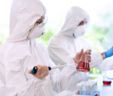 Laboratuvarda çalışan koruyucu giysi ve maskeli bilim adamları laboratuvar ekipmanları kullanıyorlardı: mikroskop, test tüpleri. İlaç, enfeksiyon ve aşı keşfi kavramı.