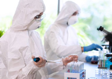 Laboratuvarda çalışan koruyucu giysi ve maskeli bilim adamları laboratuvar ekipmanları kullanıyorlardı: mikroskop, test tüpleri. Biyolojik tehlike, farmasötik keşif, bakteri ve virüs bilimi kavramı.