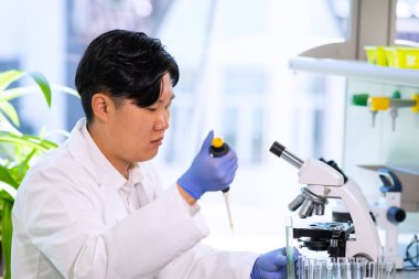 Araştırma laboratuarında çalışan Asyalı tıp doktoru. İlaç deneyleri yapan bilim asistanı. Laboratuvar aletleri: mikroskop, test tüpleri, ekipmanlar. Kimya, tıp, biyokimya, biyoteknoloji