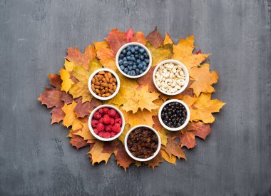 Mevsimlik sonbahar arka planı. Gri üzerinde renkli akçaağaç yaprakları, kuru üzüm, fındık ve çilek Çerçeve