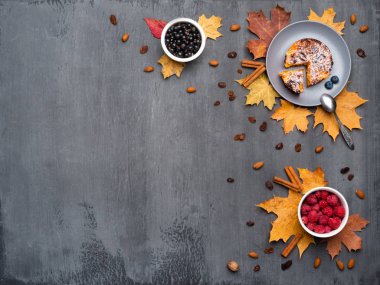 Mevsimlik sonbahar arka planı. Renkli akçaağaç yaprakları çerçeve, hindistan cevizi, kek, ahududu, siyah frenk üzümü ve gri doku üzerinde tarçın.