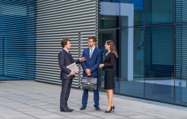 Modern ofis binasının önünde konuşan emin işadamlarının. İşadamlarının ve iş kadınının işi var. Bankacılık, profesyonel iş ve finansal piyasa konsepti.