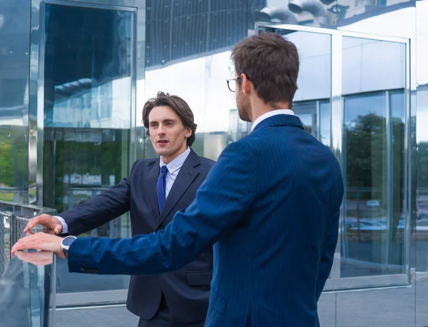 Des hommes d'affaires confiants qui parlent devant un immeuble de bureaux moderne. Homme d'affaires et son collègue. Banques et marchés financiers . — Photo