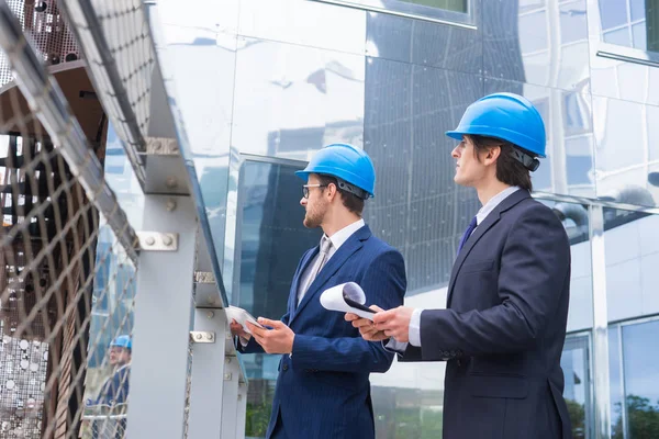 Real estate developers in helmets. New office construction. Confident business men and architect talking in front of modern office building. — Stock Photo, Image