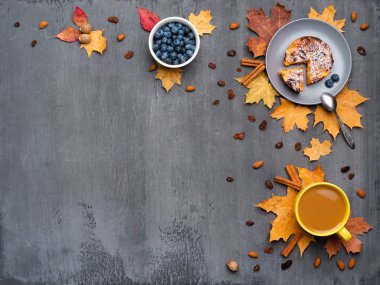 Mevsimlik sonbahar arka planı. Çerçeve renkli akçaağaç yaprakları ve sıcak içecek, kahve, latte veya kapuçino, hindistan cevizi, kek, yaban mersini ve tarçın gri üzerinde bir fincan.