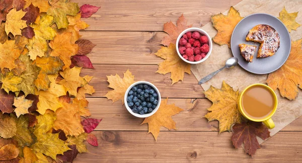 Saisonaler Herbst Hintergrund. Rahmen aus Ahornblättern und einem Kuchen und Beeren auf Holzgrund. — Stockfoto