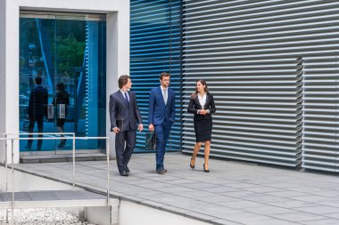 Kendine güvenen iş adamları modern ofis binasının önünde konuşuyorlar. İş adamları ve iş kadını iş görüşmesi. Bankacılık ve finans piyasası kavramı.