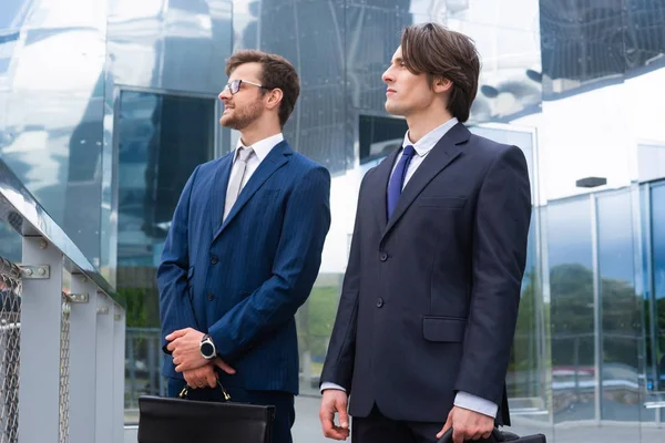 Kendine güvenen iş adamları modern ofis binasının önünde konuşuyorlar. İş adamı ve iş arkadaşı. Bankacılık ve finans piyasası.