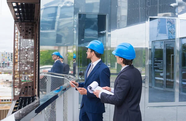 Immobilienentwickler in Helmen. Büroneubau. Selbstbewusste Geschäftsleute und Architekten im Gespräch vor modernen Bürogebäuden. — Stockfoto