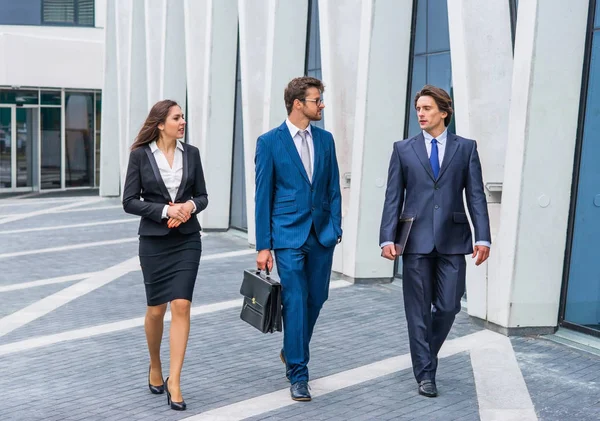 Empresarios confiados hablando frente a un moderno edificio de oficinas. Los hombres de negocios y la mujer de negocios tienen una conversación de negocios. Concepto de mercado bancario y financiero . — Foto de Stock