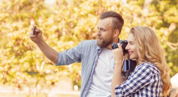Man och kvinna tar foton med en kamera och en smartphone i höst parken. — Stockfoto