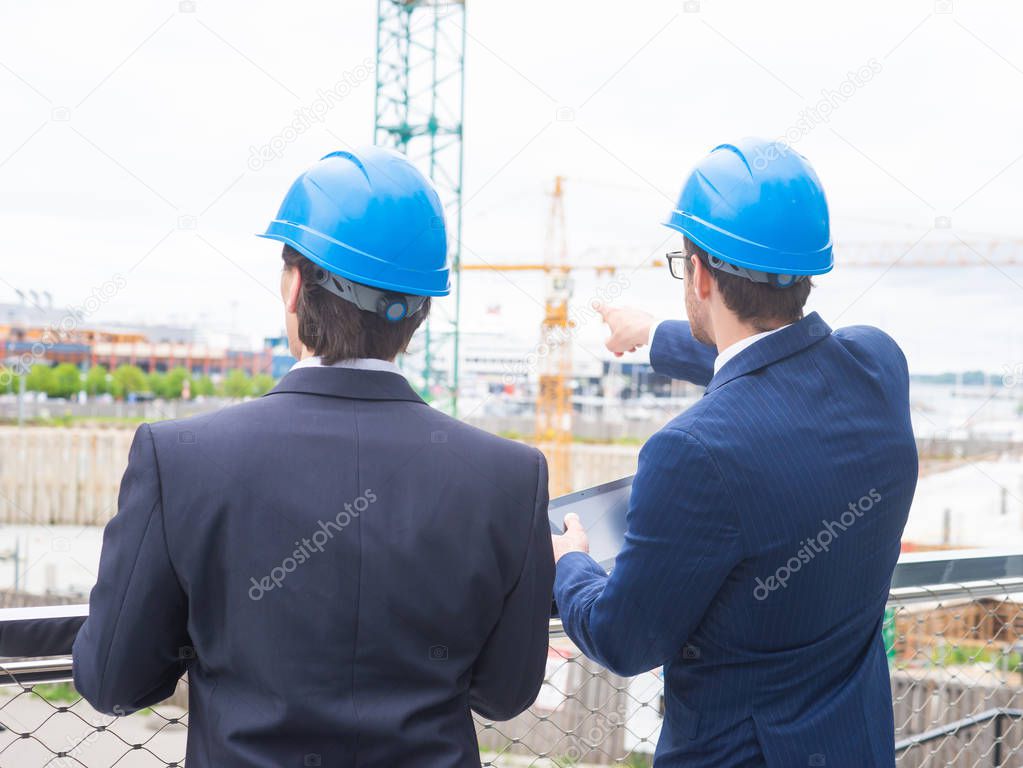 Real estate developers in helmets. New office construction. Confident business men and architect talking in front of modern office building.