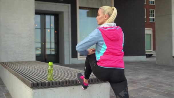 Menina loira jovem, atraente e desportiva fazendo exercícios de aquecimento ao ar livre. Saúde e estilo de vida . — Vídeo de Stock