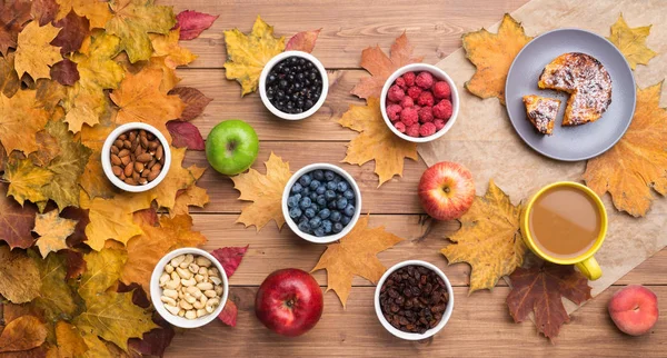 Fond saisonnier d'automne. Cadre de feuilles d'érable et un gâteau, baies, raisins secs, pommes, fruits, café et noix sur fond en bois . — Photo
