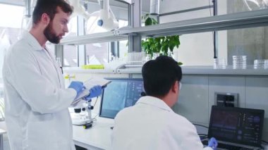 Laboratuvarda çalışan bilim adamı ve asistanı. Doktor stajyere araştırma yapmayı öğretiyor. Laboratuvar araçları: mikroskop, test tüpleri, ekipmanlar.
