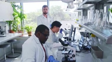 Laboratuvarda çalışan bilim adamları ve öğrenciler. Doktor stajyerlere araştırma yapmayı öğretiyor. Laboratuvar aletleri: mikroskop, test tüpleri, ekipmanlar. Biyoteknoloji, kimya, bakteri, viroloji.