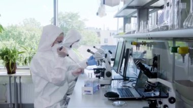 Laboratuvarda çalışan koruyucu giysi ve maskeli bilim adamları laboratuvar ekipmanları kullanıyorlardı: mikroskop, test tüpleri. Biyolojik tehlike, farmasötik keşif, bakteri ve viroloji.