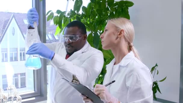 Vetenskapsmannen och hans assistent arbetar i labbet. Läkare som lär praktikanter att analysera forskning. Laboratorieverktyg: mikroskop, provrör, utrustning. — Stockvideo