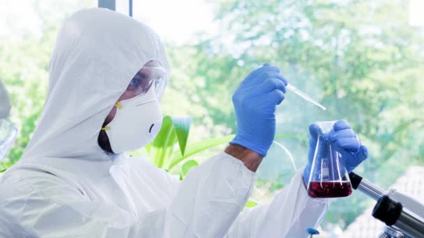 身穿防护服和戴口罩的科学家使用实验室设备在研究实验室工作：显微镜、试管。 生物危害、药物发现、细菌学和病毒学. — 图库视频影像