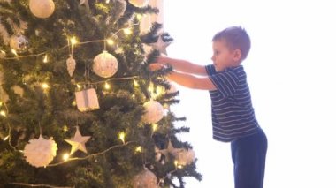 Çekici küçük çocuk Noel ağacını toplar ve ışıklarla süslüyor. Çocuk evde yeni yıla hazırlanıyor..