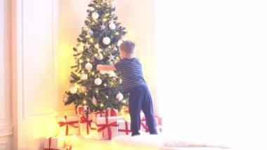 Çekici küçük çocuk Noel ağacını toplar ve ışıklarla süslüyor. Çocuk evde yeni yıla hazırlanıyor..