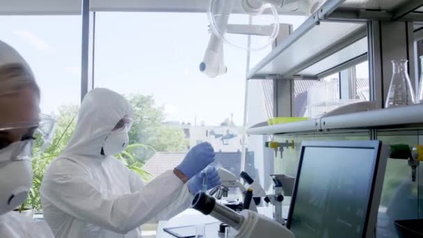 Науковці в галузі захисту костюмів і масок, що працюють в науково-дослідній лабораторії, використовують лабораторне обладнання: мікроскопи, пробірки. Біологічна небезпека, фармацевтичні відкриття, бактеріологія та вірусологія . — стокове відео
