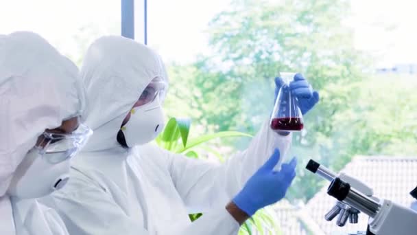 Scientists in protection suits and masks working in research lab using laboratory equipment: microscopes, test tubes. Biological hazard, pharmaceutical discovery, bacteriology and virology. — Stock Video