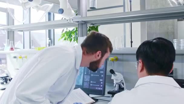 Scientist and his assistant working in lab. Doctor teaching intern to make analyzing research. Laboratory tools: microscope, test tubes, equipment. — Stock Video