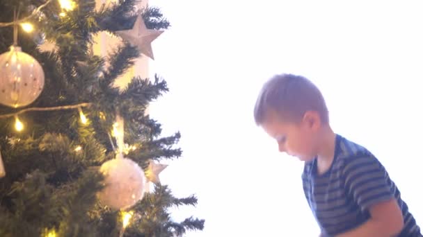 ボールやライトでクリスマスツリーを飾る魅力的な小さな男の子。家で新年の準備をする子供. — ストック動画