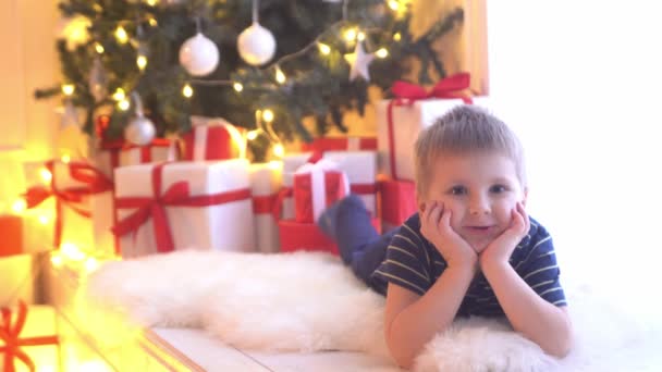 Atractivo niño desenvolviendo regalos de Navidad. El niño abre los regalos de Año Nuevo en casa . — Vídeo de stock