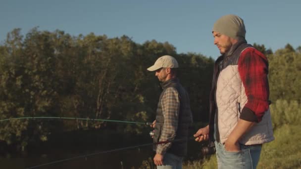 Fishermen friends with a spinning rod catching fish on a river. Fisher men on a weekend. Hobby, leisure and active summer and autumn concept. — ストック動画