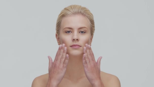 Retrato de estudio de mujer rubia joven, hermosa y natural que aplica crema para el cuidado de la piel. Levantamiento facial, cosméticos y maquillaje . — Vídeo de stock