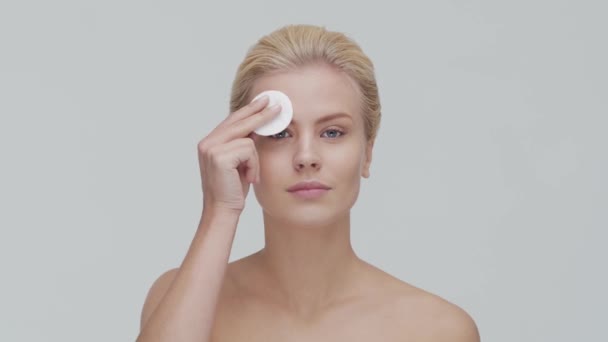 Studio porträtt av ung, vacker och naturlig blond kvinna som tillämpar hudvård grädde. Ansiktslyftning, kosmetika och make-up. — Stockvideo