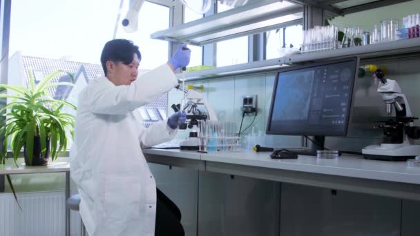 아시아의 과학자 가 연구실에서 일하고 있습니다. 미생물학 연구를 하는 의사. 실험실 도구: 현미경, 시험관, 장비. 생명 공학, 화학, 세균학, 바이러스학. — 비디오