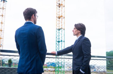 Kasklı emlak çırakları. Yeni ofis inşaatı. Kendine güvenen iş adamları ve mimar modern ofis binası önünde konuşuyor.