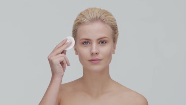 Studioporträt einer jungen, schönen und natürlichen blonden Frau, die Hautpflegecreme aufträgt. Gesichtslifting, Kosmetik und Make-up. — Stockvideo