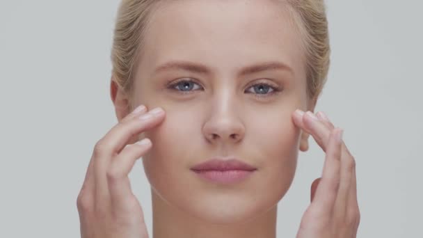 Retrato de estudio de mujer rubia joven, hermosa y natural que aplica crema para el cuidado de la piel. Levantamiento facial, cosméticos y maquillaje . — Vídeo de stock