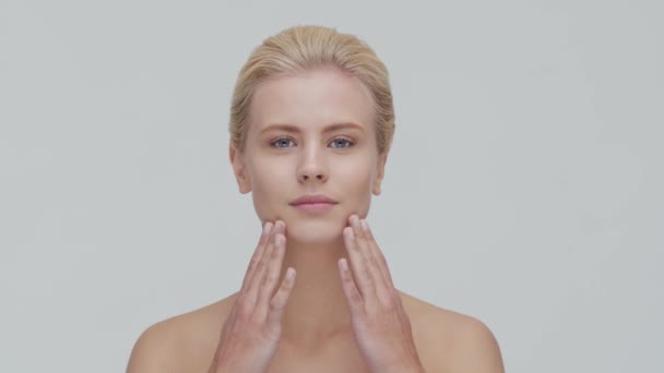 Studio portret van jonge, mooie en natuurlijke blonde vrouw die huidverzorgingscrème aanbrengt. Gezichtsheffen, cosmetica en make-up. — Stockvideo