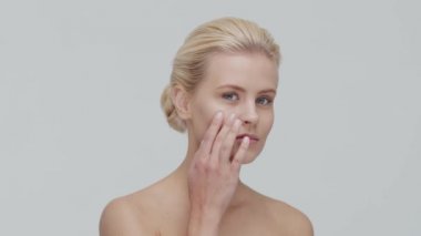 Cilt bakımı kremi süren genç, güzel ve doğal sarışın kadının stüdyo portresi. Yüz gerdirme, makyaj ve makyaj malzemeleri..