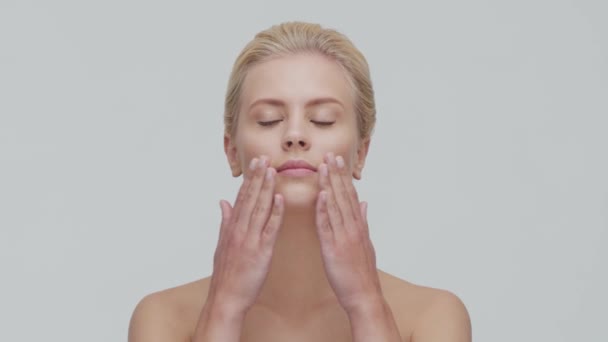 Studio ritratto di giovane, bella e naturale donna bionda che applica la crema per la cura della pelle. lifting viso, cosmetici e make-up . — Video Stock