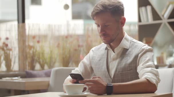 Affärsman som sitter och arbetar på ett café. Man som använder mobila enheter. Företag och entreprenörskap. — Stockvideo
