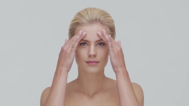 Studio portret van jonge, mooie en natuurlijke blonde vrouw die huidverzorgingscrème aanbrengt. Gezichtsheffen, cosmetica en make-up. — Stockvideo