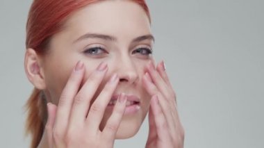 Cilt bakımı kremi süren genç, güzel ve doğal kızıl saçlı kadının stüdyo portresi. Yüz gerdirme, makyaj ve makyaj malzemeleri..