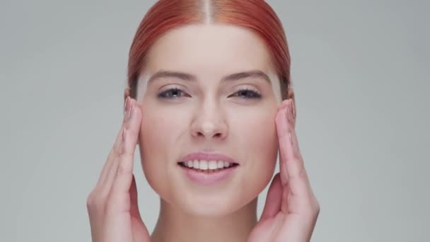 Retrato de estudio de mujer pelirroja joven, hermosa y natural aplicando crema para el cuidado de la piel. Levantamiento facial, cosméticos y maquillaje . — Vídeo de stock