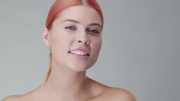 Retrato de estudio de mujer pelirroja joven, hermosa y natural aplicando crema para el cuidado de la piel. Levantamiento facial, cosméticos y maquillaje . — Vídeos de Stock