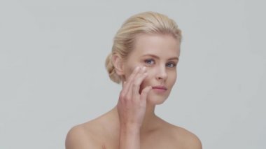 Cilt bakımı kremi süren genç, güzel ve doğal sarışın kadının stüdyo portresi. Yüz gerdirme, makyaj ve makyaj malzemeleri..