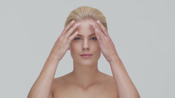 Retrato de estudio de mujer rubia joven, hermosa y natural que aplica crema para el cuidado de la piel. Levantamiento facial, cosméticos y maquillaje . — Vídeos de Stock