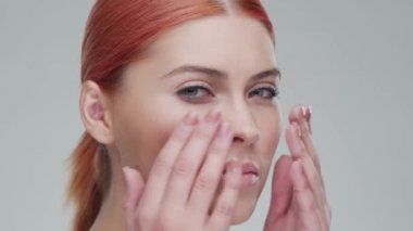 Cilt bakımı kremi süren genç, güzel ve doğal kızıl saçlı kadının stüdyo portresi. Yüz gerdirme, makyaj ve makyaj malzemeleri..