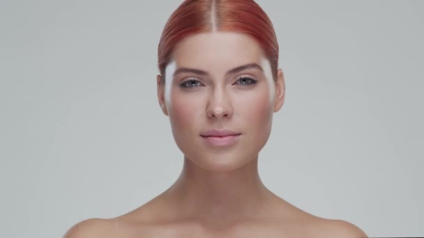 Retrato de estudio de mujer pelirroja joven, hermosa y natural aplicando crema para el cuidado de la piel. Levantamiento facial, cosméticos y maquillaje . — Vídeo de stock